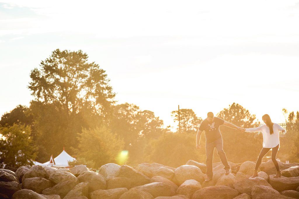 A couple holds hands as they walk across the rocks at sunset