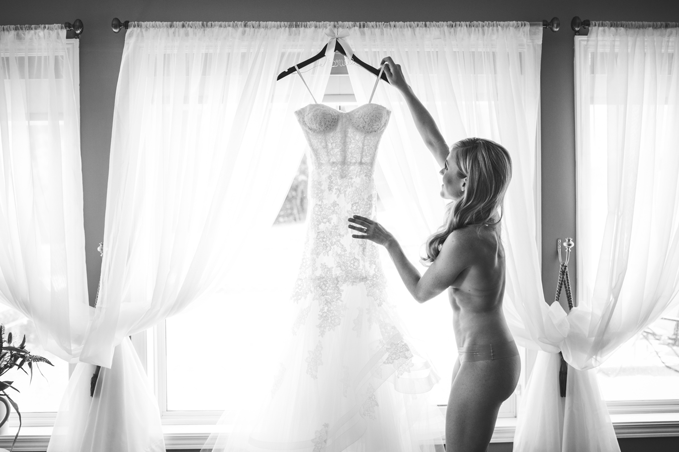 nude bride removes wedding dress from hanger