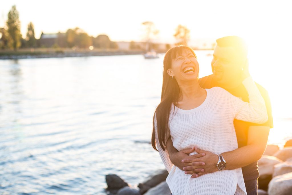 A couple laughs together as the sun sets over the city of Vancouver, during their engagement portraits