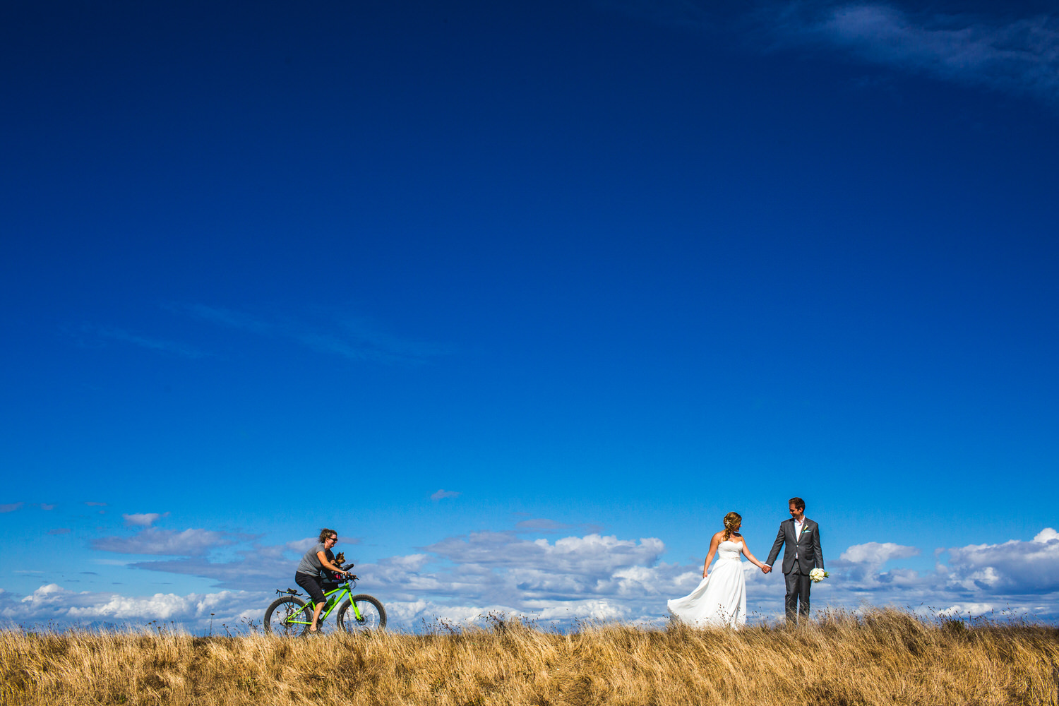 cyclists passes by bride and groom at beach