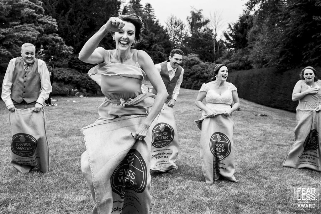 A wedding party having a potato sack race, a bridesmaid has her first in the air and is a few feet ahead of everyone else.